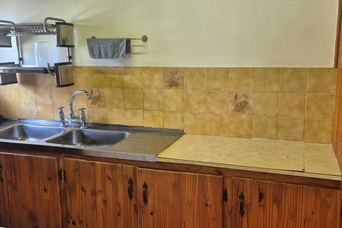 A functional kitchen area featuring traditional wooden cabinetry, a double stainless steel sink, and a tiled backsplash with a laminate countertop.