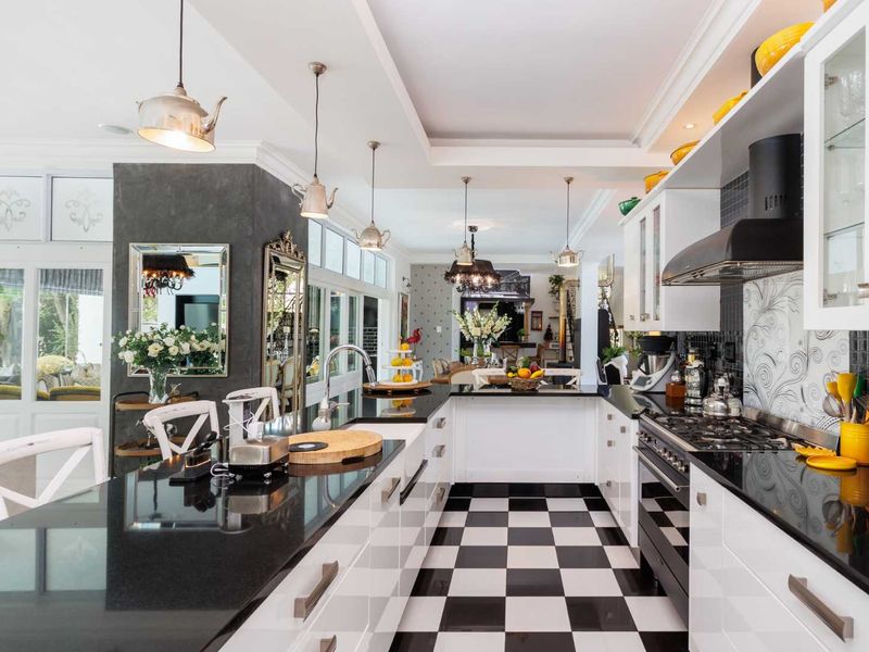 A modern, high-contrast kitchen featuring black granite countertops, white high-gloss cabinetry, a gas cooktop, and distinctive checkered floor tiles.