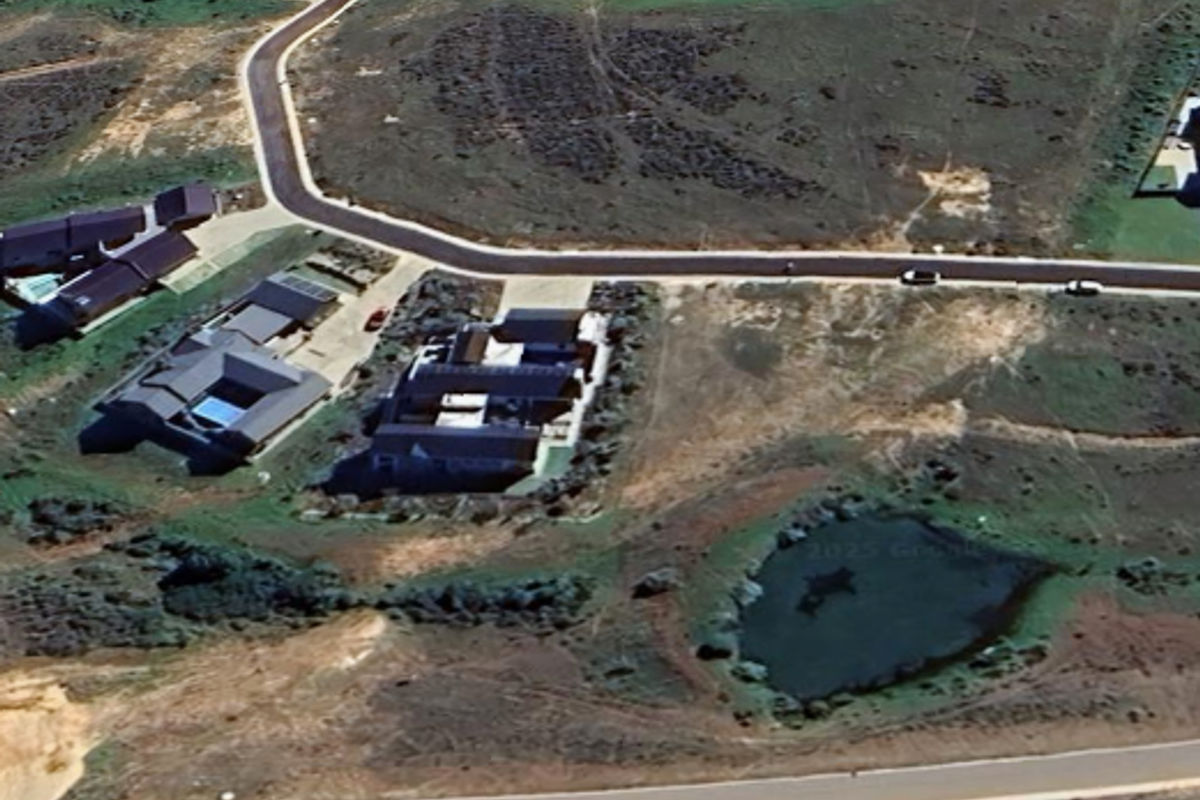 Aerial view of a residential estate featuring paved roads, established homes, and a natural pond within a developing landscape.