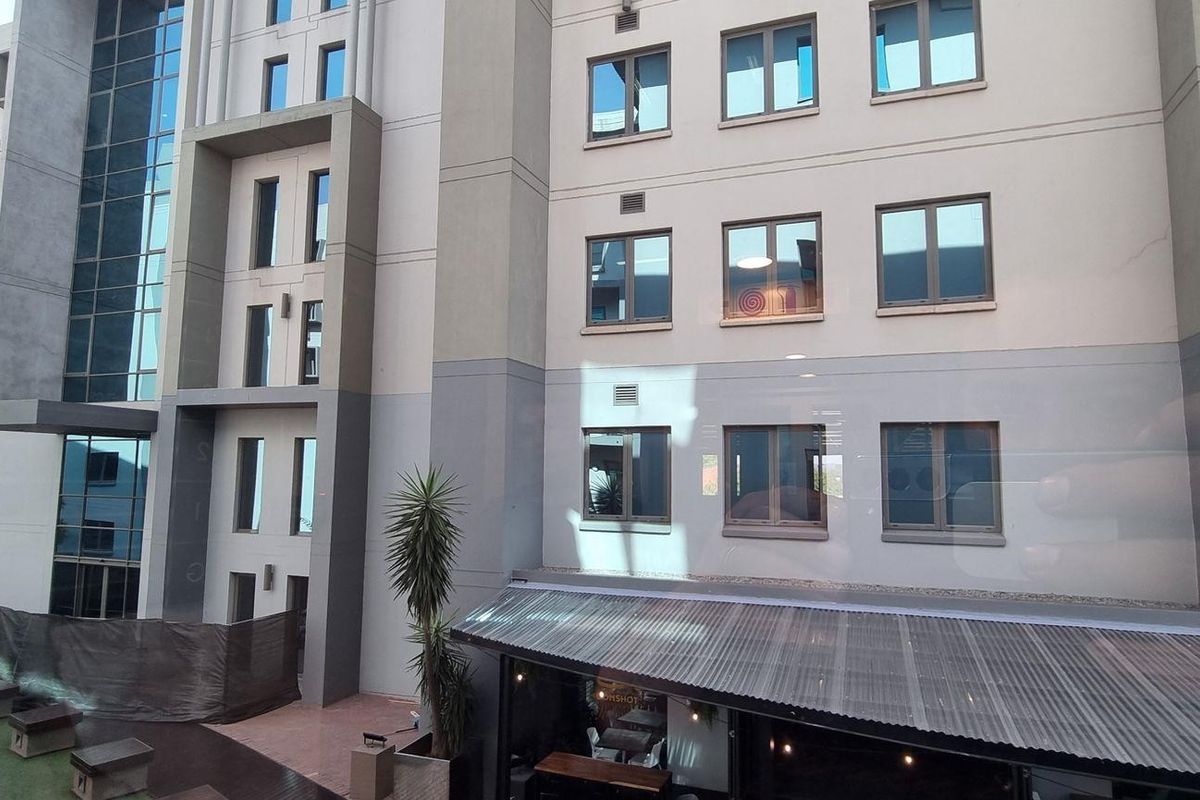 Exterior view of a modern multi-story office building featuring a combination of glass curtain walls, concrete facade elements, and a ground-level covered patio area.