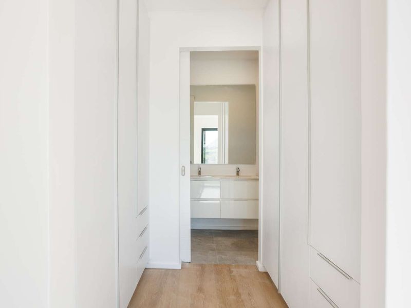 A bright, minimalist hallway featuring extensive built-in floor-to-ceiling cabinetry, leading through a sliding door into a modern bathroom.