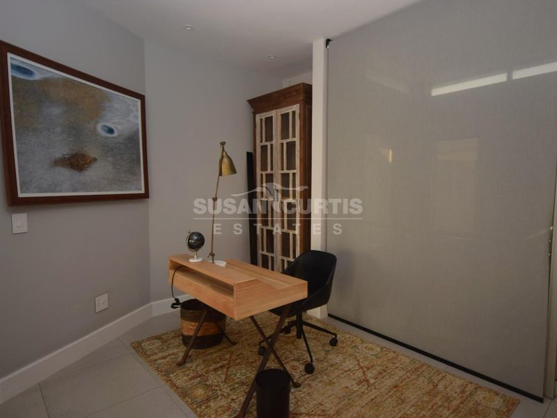 A modern home office space featuring neutral grey walls, tiled flooring, and a large sliding glass partition for flexible room division.