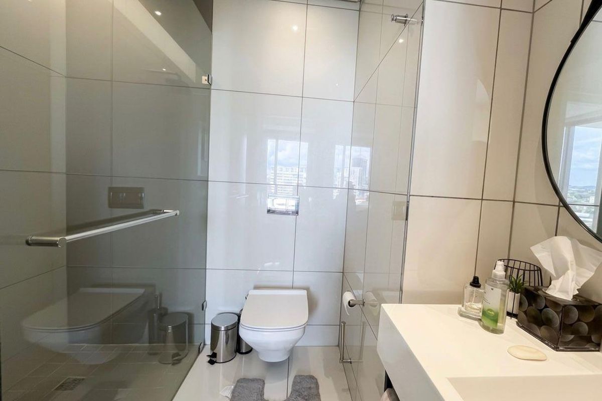 Modern bathroom featuring a wall-mounted toilet, glass-enclosed walk-in shower with rainfall showerhead, and a sleek vanity basin with large format wall tiles.