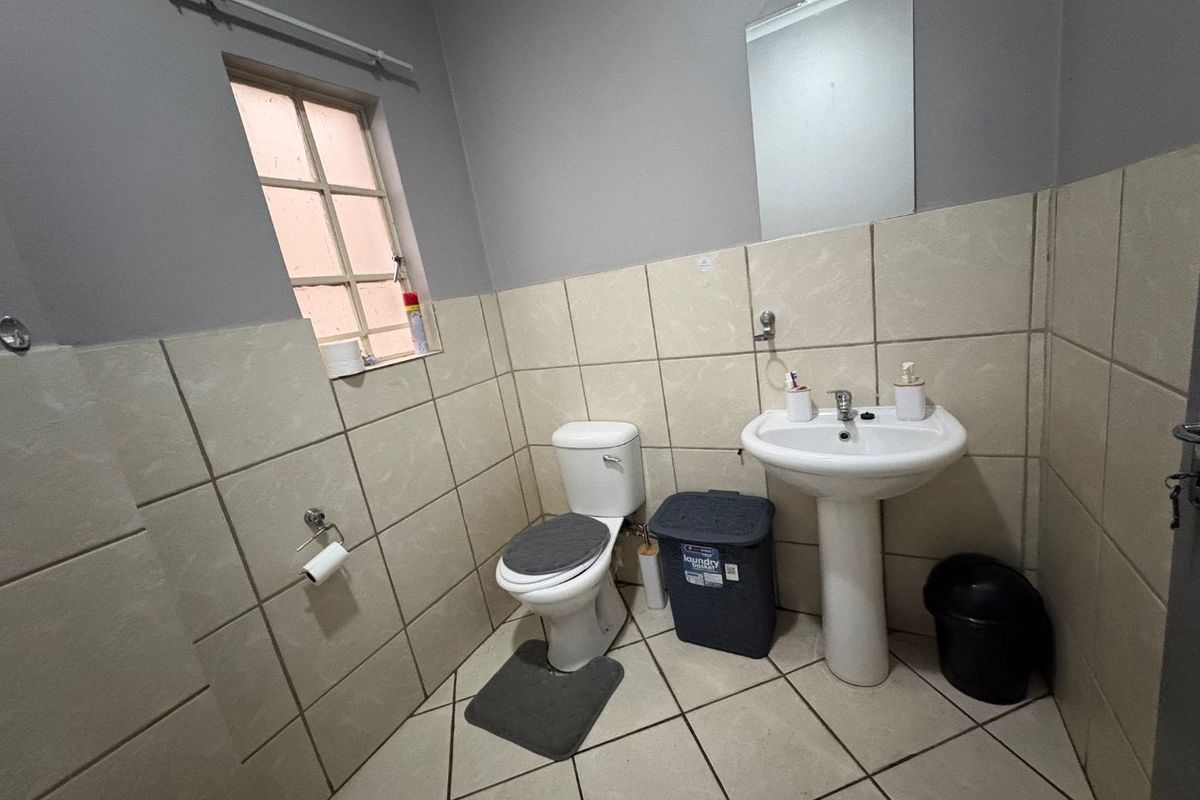 A functional bathroom featuring a pedestal washbasin, toilet, wall-mounted mirror, and neutral ceramic tiling throughout.