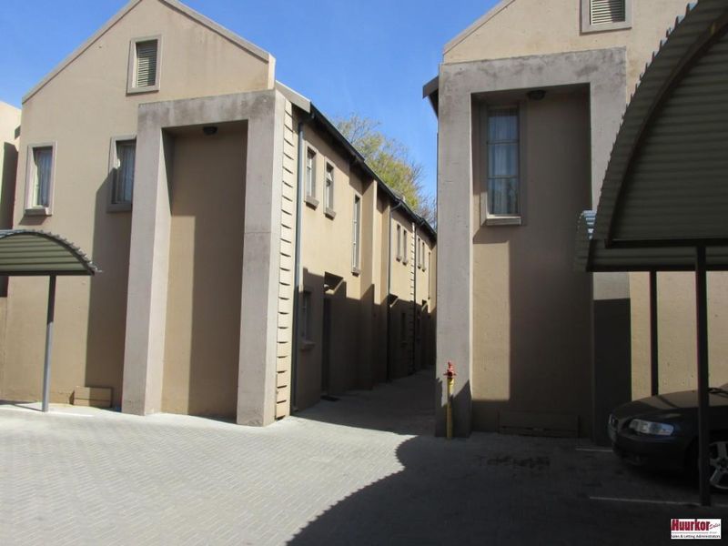 Exterior view of the apartment complex featuring a paved driveway, covered parking bays, and modern stucco facade architecture.