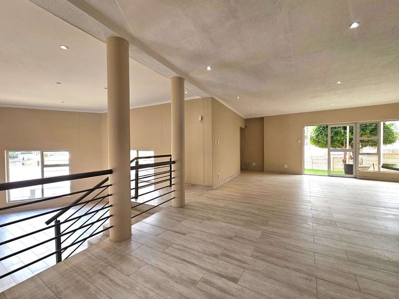 Spacious open-plan living area featuring modern tiled flooring, structural columns, a metal balustrade overlooking the lower level, and large sliding doors to the garden.