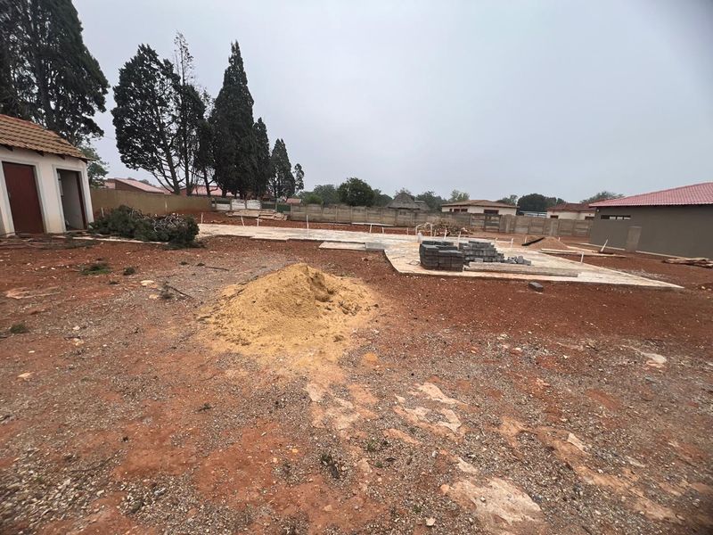 A view of a residential plot under development, featuring a concrete foundation slab, boundary walls, and an existing outbuilding structure.