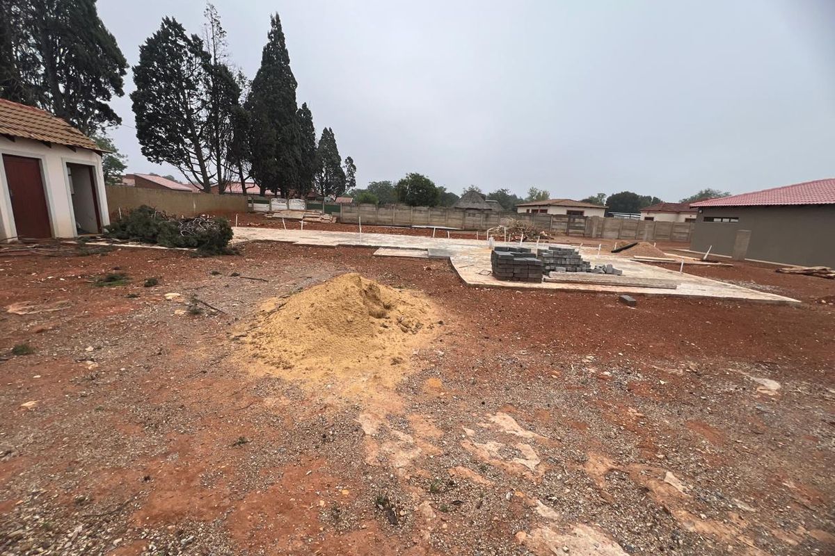 A view of a residential plot under development, featuring a concrete foundation slab, boundary walls, and an existing outbuilding structure.