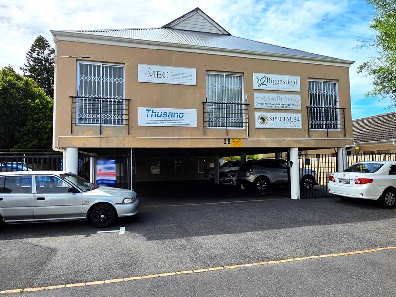 Front elevation of a two-story office building featuring ground-level covered parking, exterior signage, and security gates.