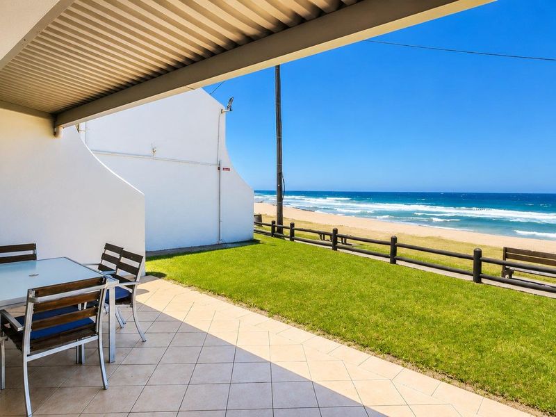 A covered patio area featuring tiled flooring and direct access to a lawn with unobstructed ocean and beach views.