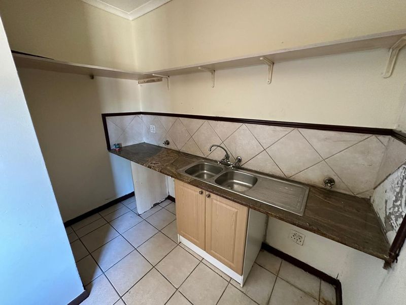 A functional scullery or utility area featuring a double bowl sink, stone countertop, tiled backsplash, and open shelving, requiring cosmetic updates.