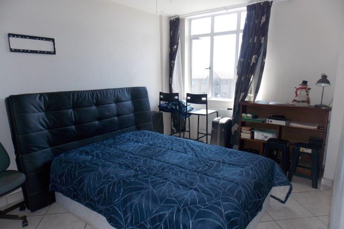A functional bedroom featuring tiled flooring, a large window providing natural light, and a ceiling fan.