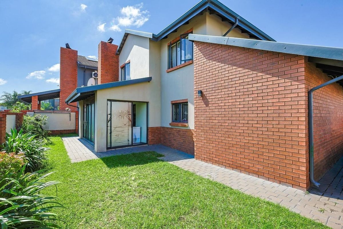Rear view of the house featuring a brick facade, paved patio area, and well-maintained lawn with established garden borders.