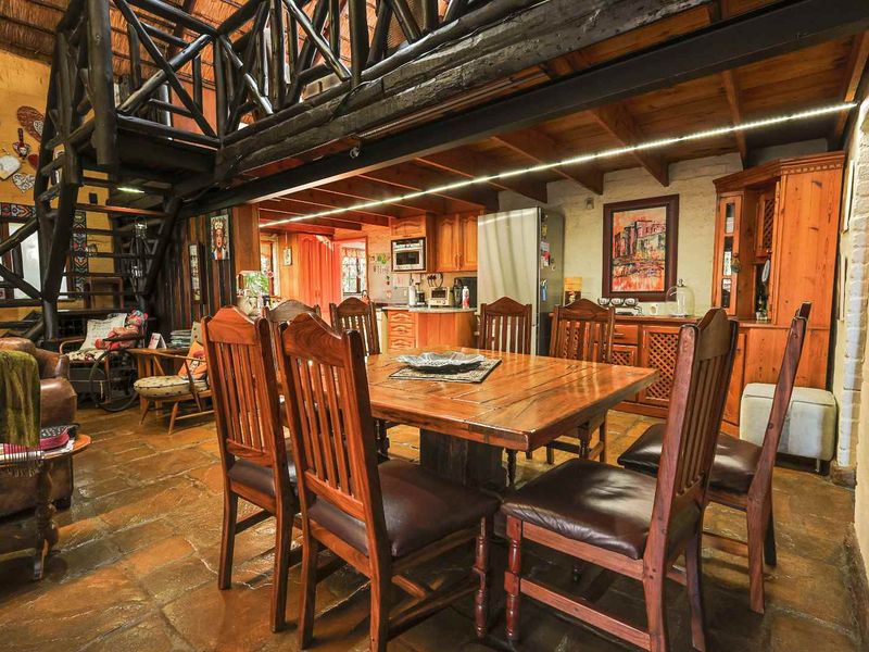 Open-plan living and dining area featuring rustic stone flooring, exposed timber ceiling beams, and a mezzanine level with wooden balustrades.