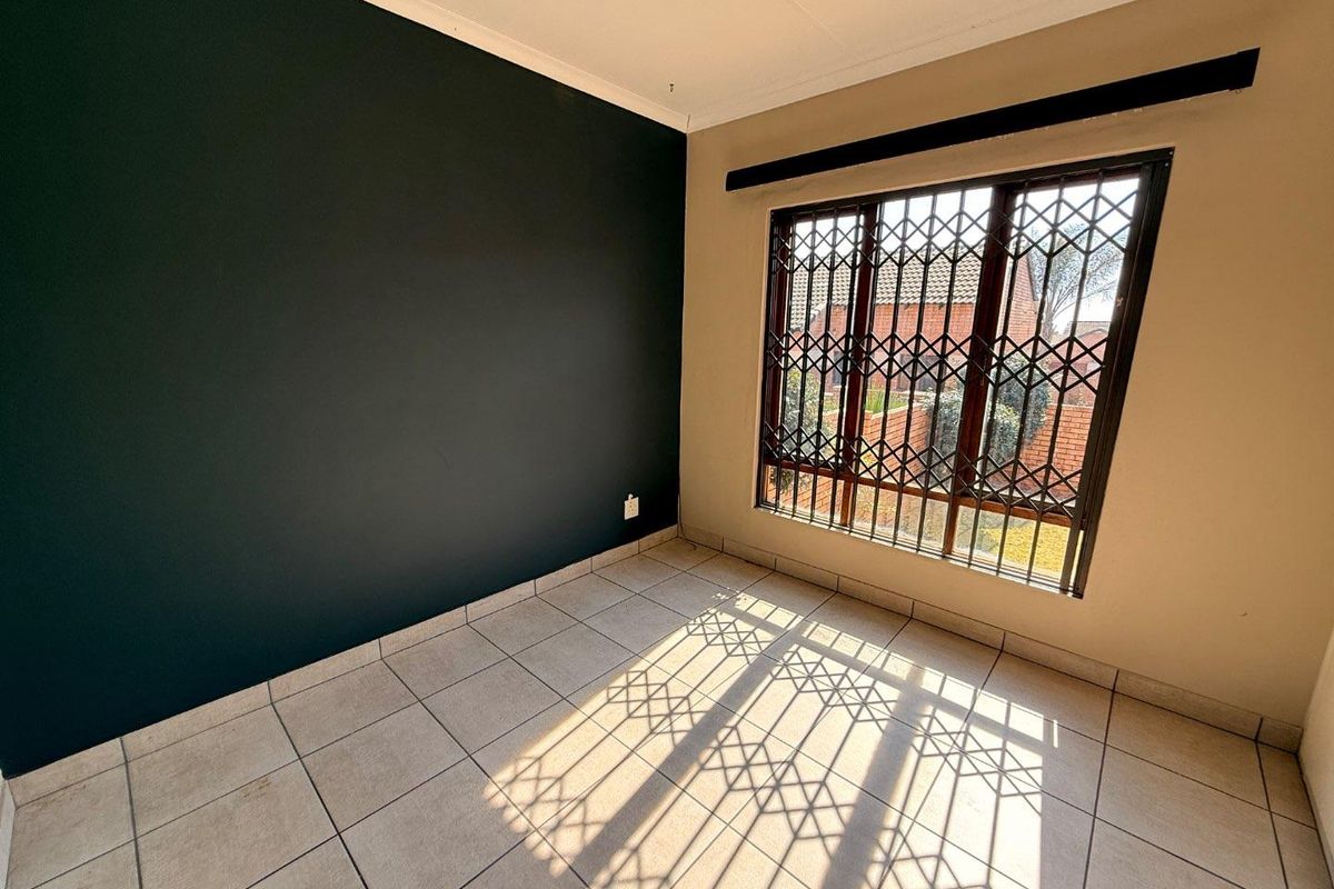 An empty bedroom featuring tiled flooring, a dark accent wall, and a window fitted with a security gate.