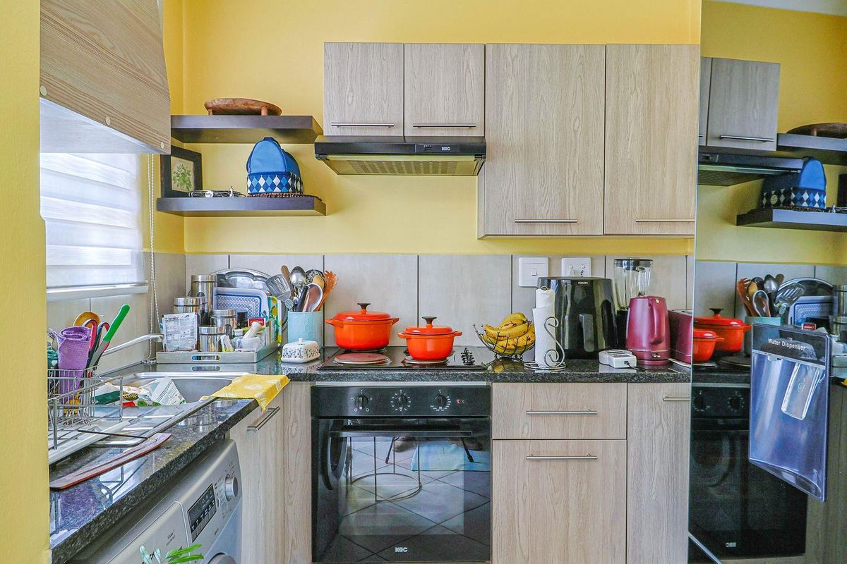 Compact kitchen featuring light wood-grain cabinetry, dark granite countertops, a built-in oven, electric hob, and an extractor fan.