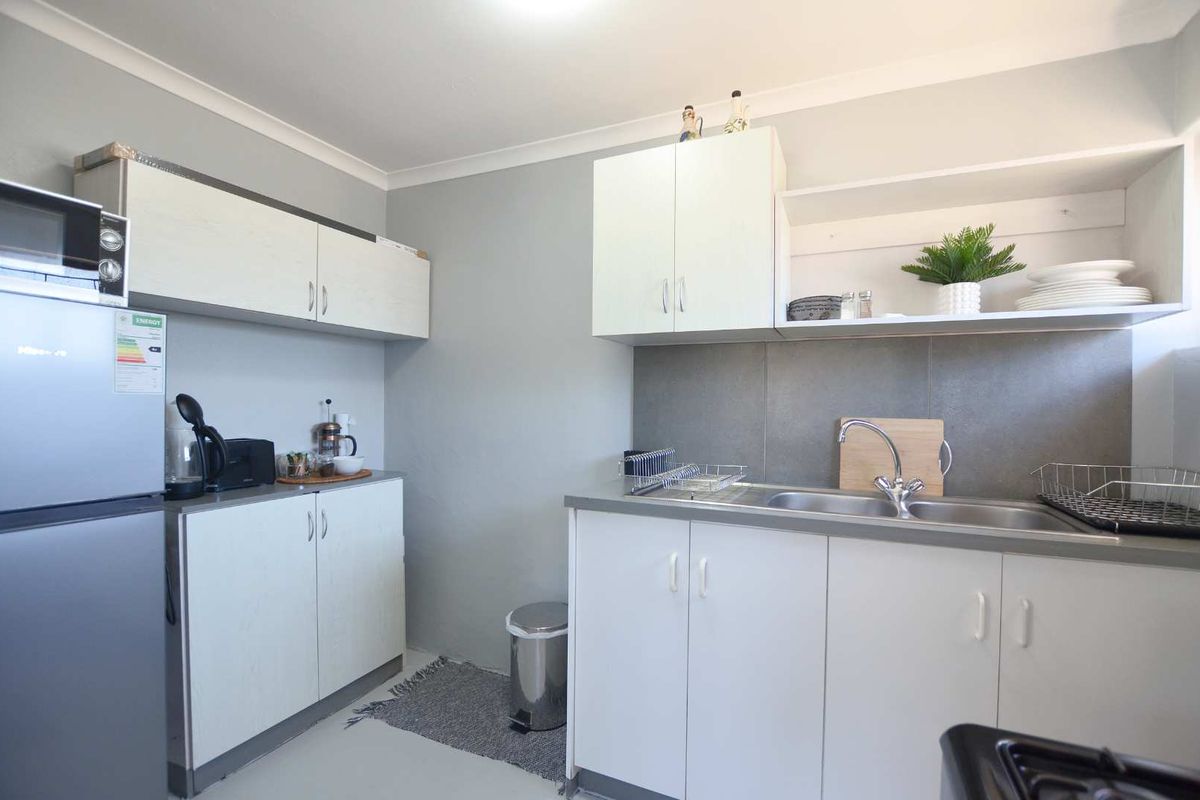 A functional kitchen featuring white built-in cabinetry, a stainless steel sink with mixer tap, and a neutral tiled splashback.