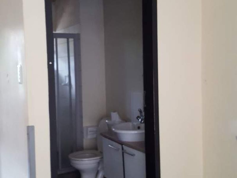 A view into a small bathroom featuring a toilet, vanity basin, and shower enclosure with tiled flooring and visible wall damage.