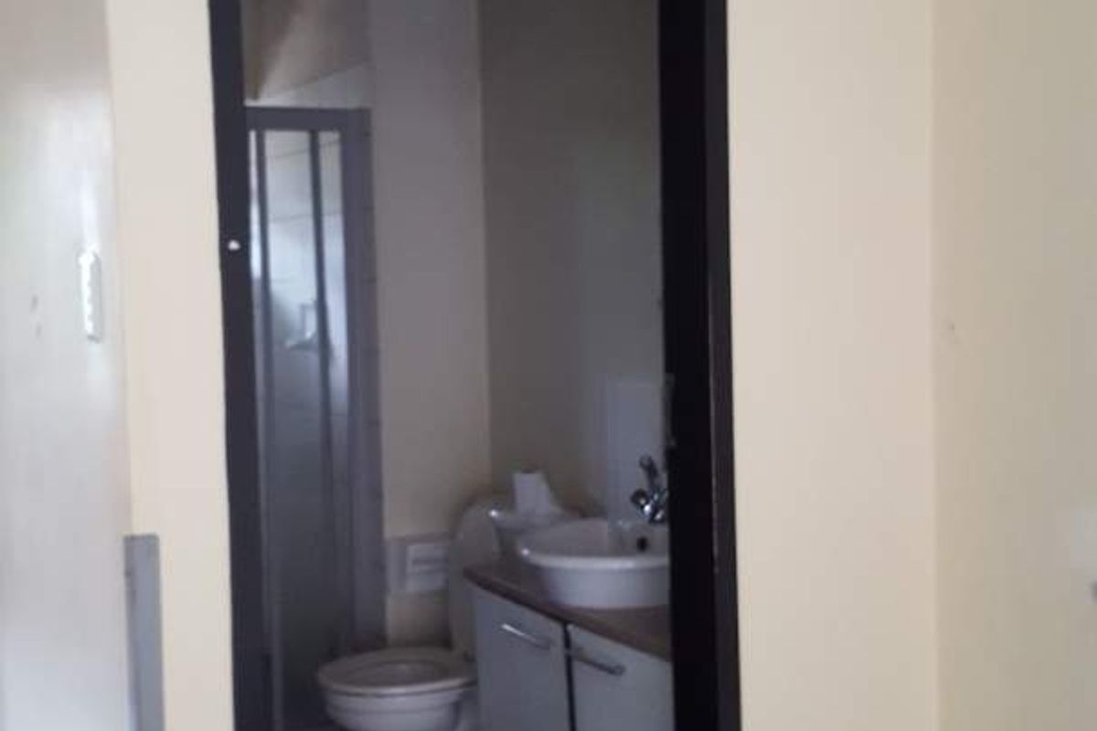 A view into a small bathroom featuring a toilet, vanity basin, and shower enclosure with tiled flooring and visible wall damage.