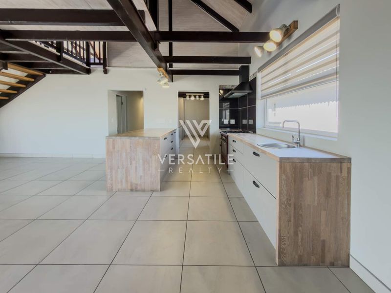 Spacious open-plan kitchen and living area featuring exposed timber beams, modern cabinetry, a central island, and tiled flooring throughout.
