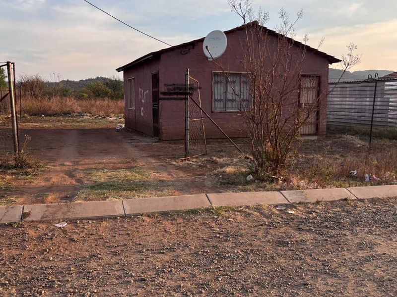 A detached single-story house featuring a basic exterior, security bars, and a satellite dish, situated on an unpaved lot with perimeter fencing.