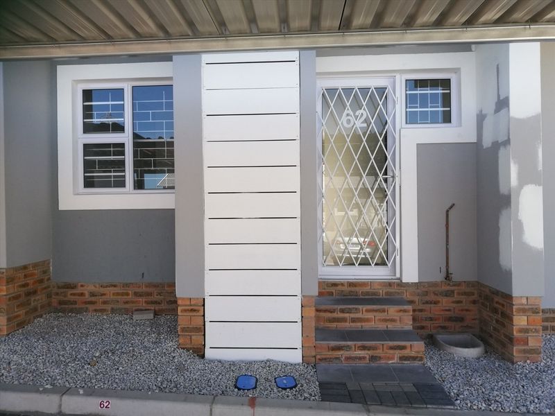 Front entrance of the apartment featuring a security gate, brick base detailing, and gravel landscaping, with some areas requiring final paint touch-ups.