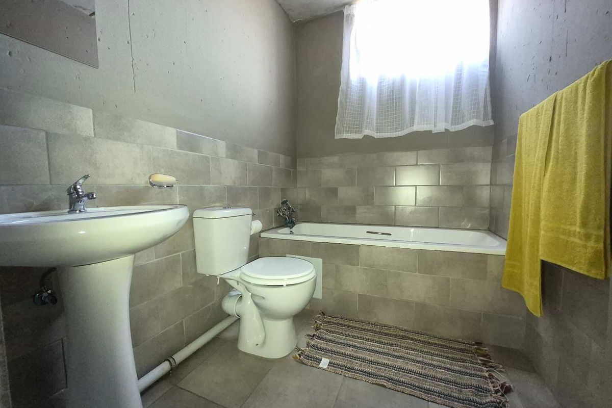 A functional bathroom featuring a pedestal basin, toilet, and bathtub with neutral wall tiling and natural light from a window.
