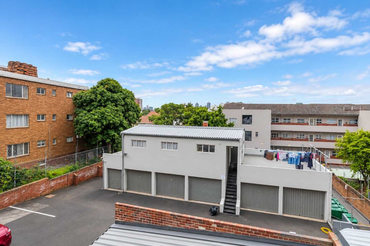 An elevated view of the rear property area featuring a multi-bay garage block with an external staircase and paved driveway.