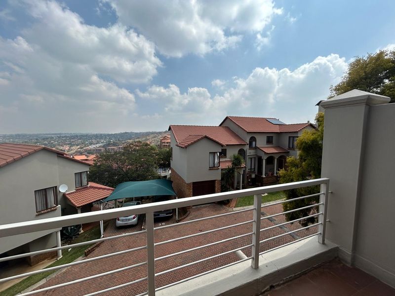 An elevated balcony view overlooking the townhouse complex, featuring a metal balustrade and tiled flooring with a scenic outlook over the surrounding area.