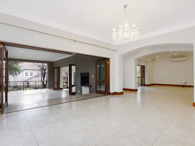 Spacious open-plan living area featuring elegant tiled floors, a crystal chandelier, and seamless flow to a covered patio through large bi-fold timber doors.