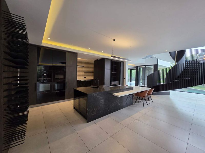 Modern open-plan kitchen featuring a large stone island, integrated appliances, and a striking spiral staircase, set within a spacious, well-lit contemporary living area.