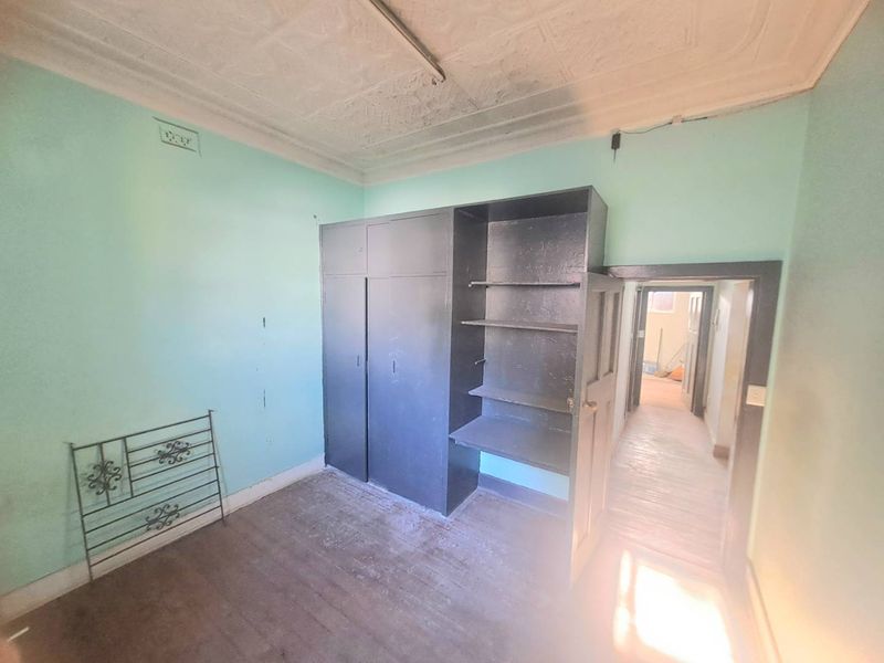 A vacant bedroom featuring original pressed metal ceilings, built-in storage cabinetry, and timber flooring, requiring cosmetic updates and refurbishment.