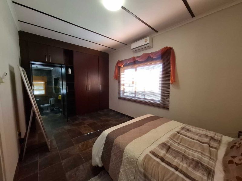A bedroom featuring dark wood built-in cupboards, tiled flooring, and an integrated split-system air conditioner, with direct access to an en-suite bathroom.
