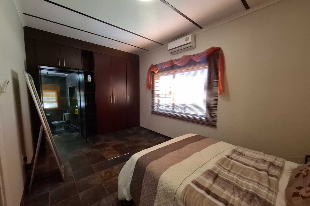 A bedroom featuring dark wood built-in cupboards, tiled flooring, and an integrated split-system air conditioner, with direct access to an en-suite bathroom.