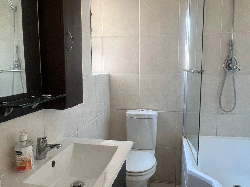 A functional bathroom featuring a vanity with basin, toilet, and a bathtub with a glass shower screen and handheld shower head.