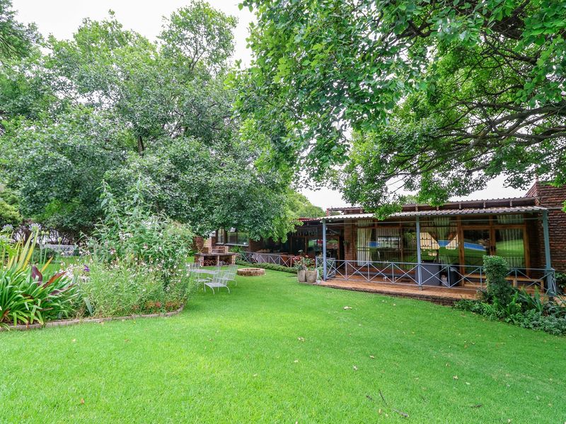 A spacious rear garden featuring a lush lawn, mature trees, and a covered patio area with a built-in brick braai.