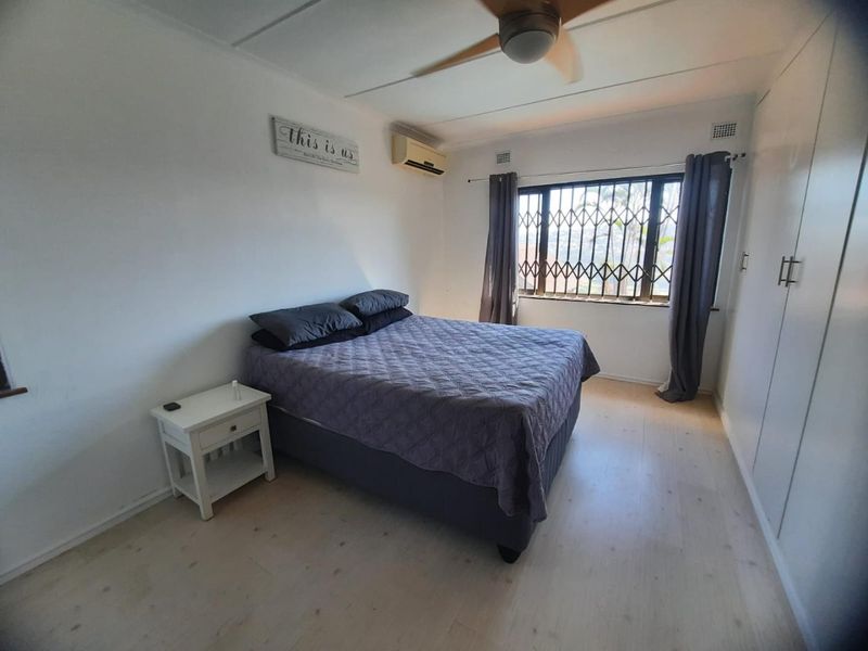 A functional bedroom featuring built-in cupboards, laminate flooring, a ceiling fan, and an air conditioning unit for climate control.