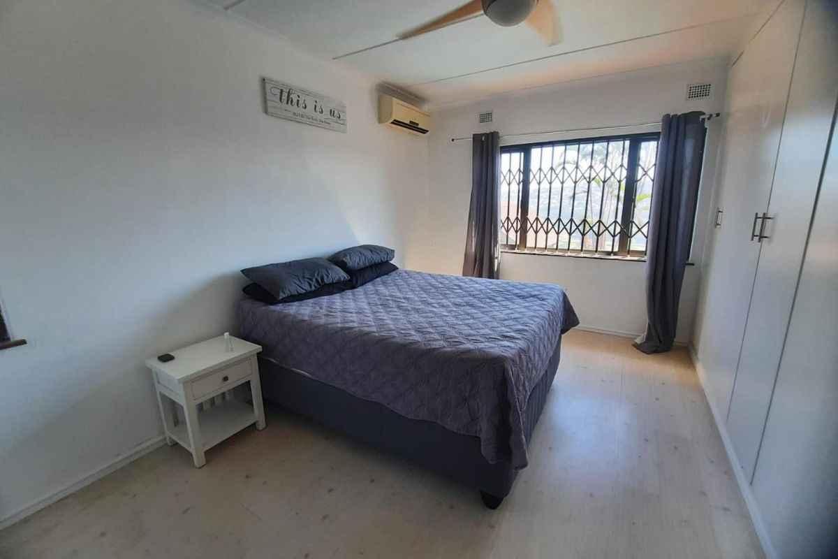 A functional bedroom featuring built-in cupboards, laminate flooring, a ceiling fan, and an air conditioning unit for climate control.