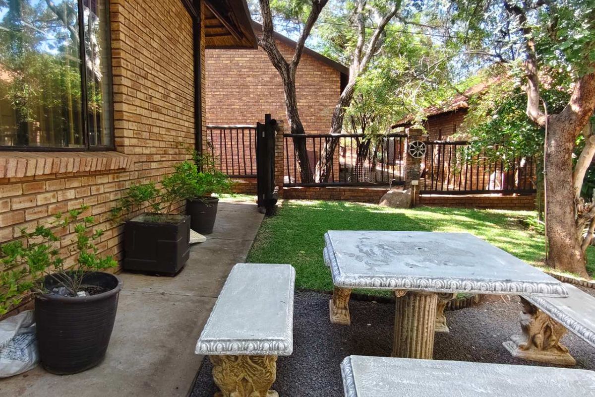 A private rear garden area featuring a paved patio, established lawn, and perimeter brick walling with metal fencing.