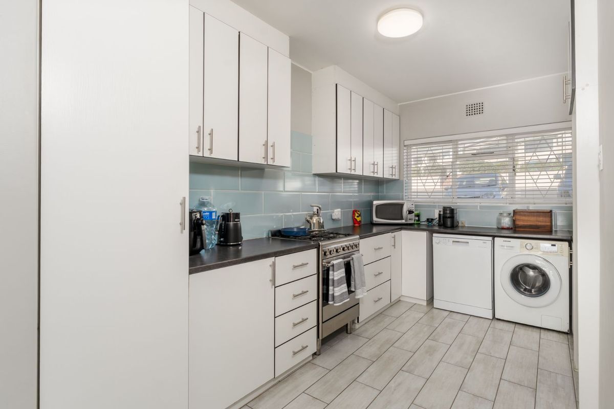 A functional kitchen featuring white cabinetry, dark countertops, light blue subway tile backsplash, and integrated appliances including a gas stove and laundry connections.