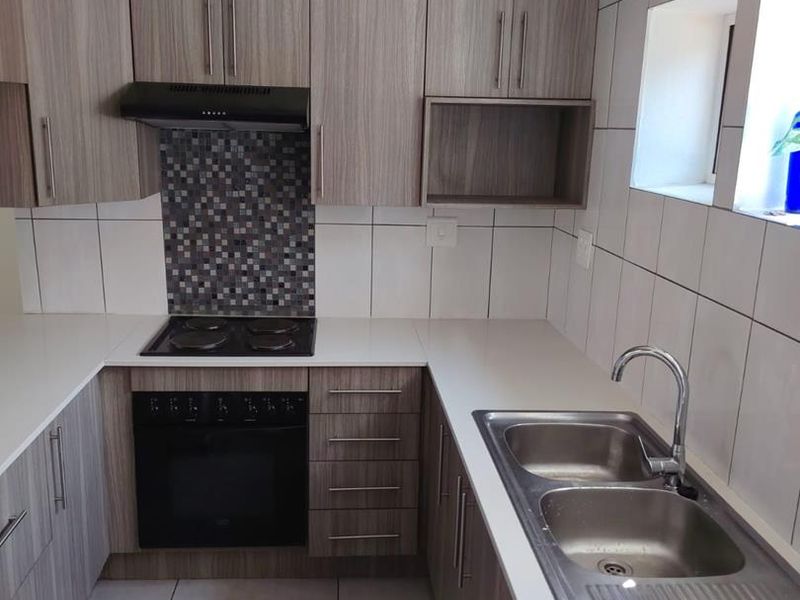 A clean, modern kitchen featuring wood-grain cabinetry, white countertops, a built-in oven with hob, and a stainless steel double sink.