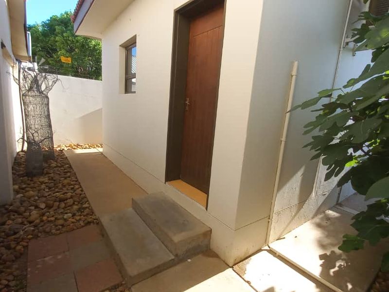 A side exterior view of the property featuring a wooden door, concrete steps, and a landscaped pebble pathway.