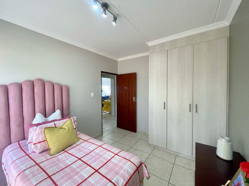 A well-maintained bedroom featuring neutral tiled flooring, a spacious built-in wardrobe, and modern track lighting.