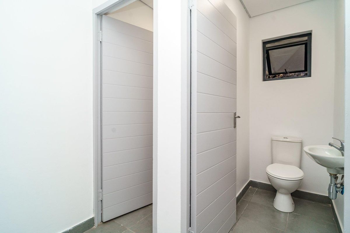 A clean, modern bathroom featuring a white toilet, wall-mounted basin, and grey tiled flooring with neutral finishes.