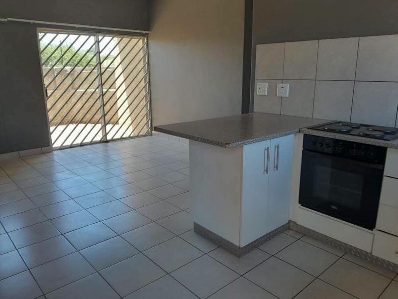 Open plan kitchen and living area featuring tiled flooring, built-in oven, hob, and direct access to an outdoor space through a security sliding door.