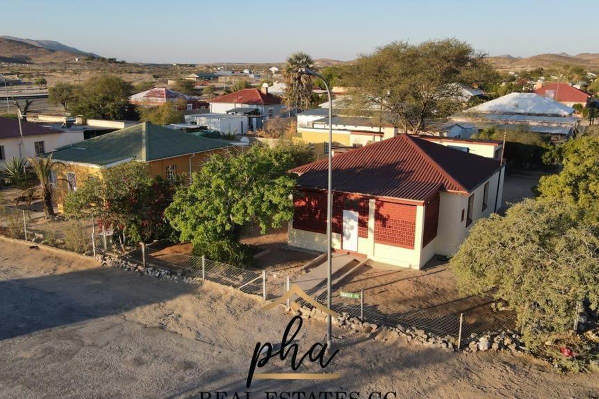 Aerial view of a residential property featuring a pitched roof house with a fenced yard in a suburban neighborhood setting.