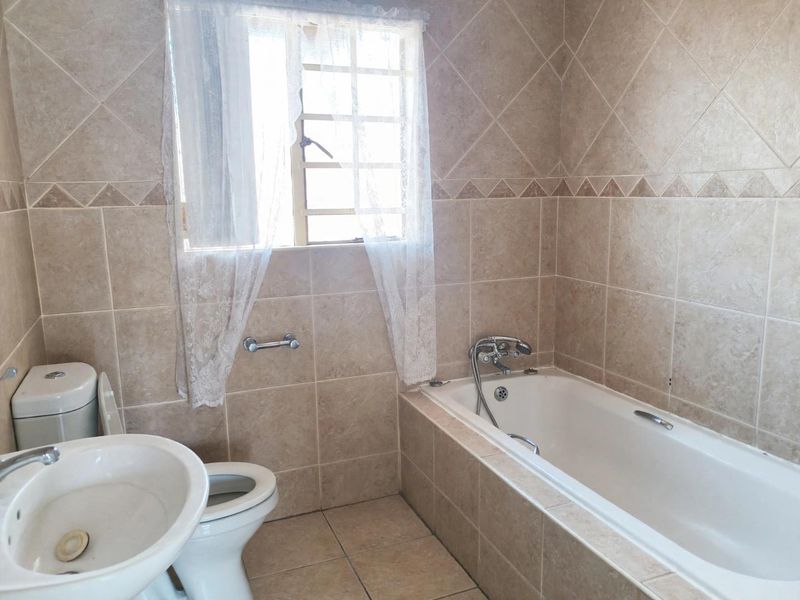 A functional bathroom featuring neutral ceramic wall and floor tiles, a built-in bathtub, a pedestal basin, and a toilet.