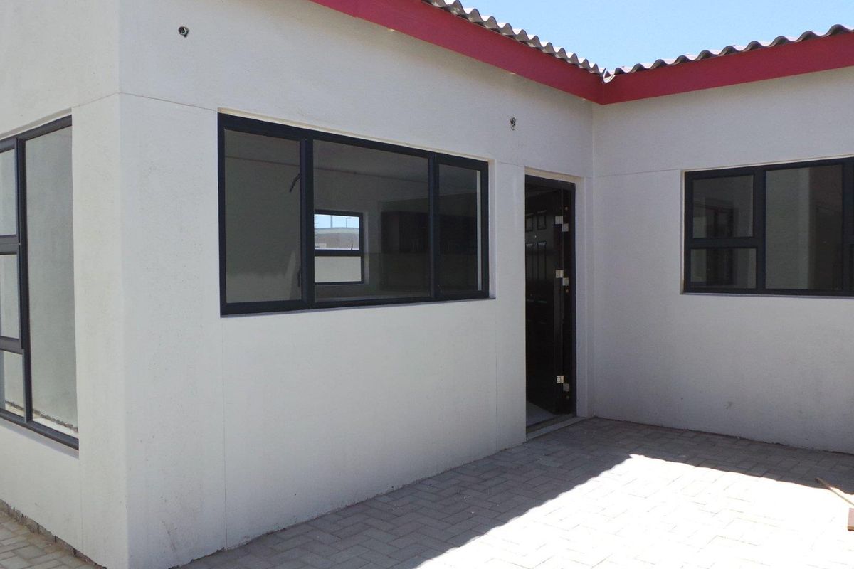 A view of the exterior rear facade featuring paved patio area, dark-framed windows, and a secure entrance door.