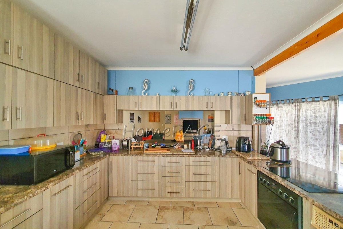 A functional U-shaped kitchen featuring light wood-grain cabinetry, granite countertops, tiled flooring, and a built-in electric oven and hob.