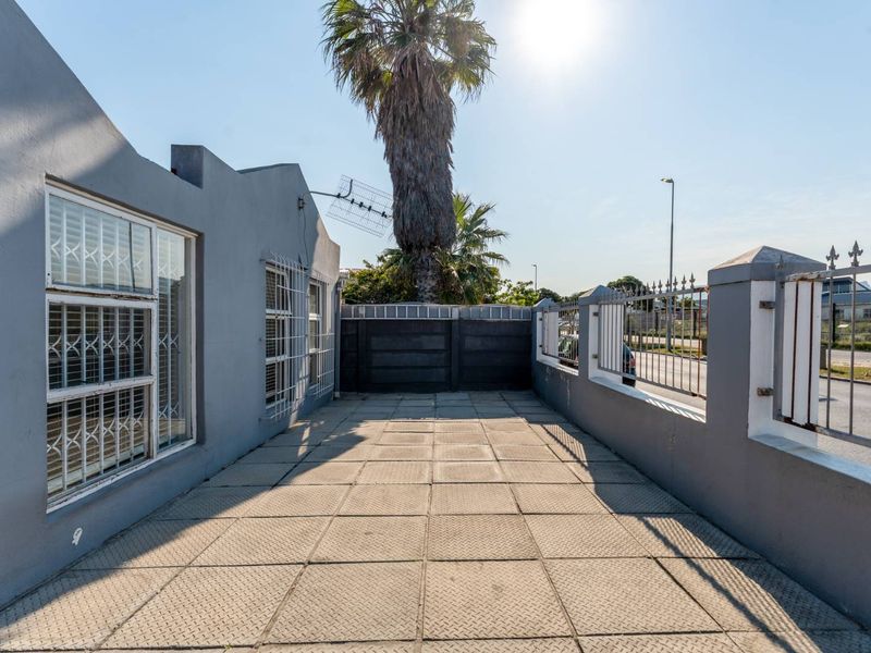 A paved front exterior area featuring a perimeter wall, security fencing, and security bars on the windows.